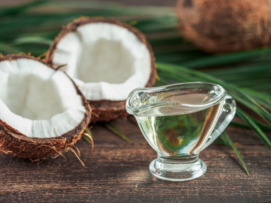 Liquid coconut oil and halved coco-nut on wooden table. 